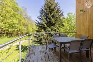 A wooden deck with a metal railing, a table with chairs, and a view of a forested area.