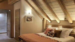 Un dormitorio con techo de madera, una cama con muchas almohadas, una mesita de noche y una puerta que da a otra habitación.