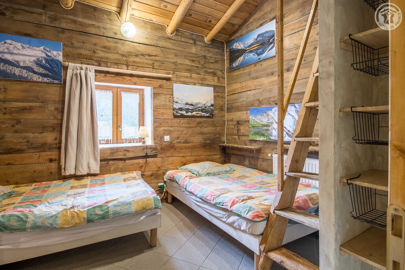 Ein gemütliches Blockhaus mit zwei Holzbetten, einem Fenster mit Vorhängen und einer Leitern.