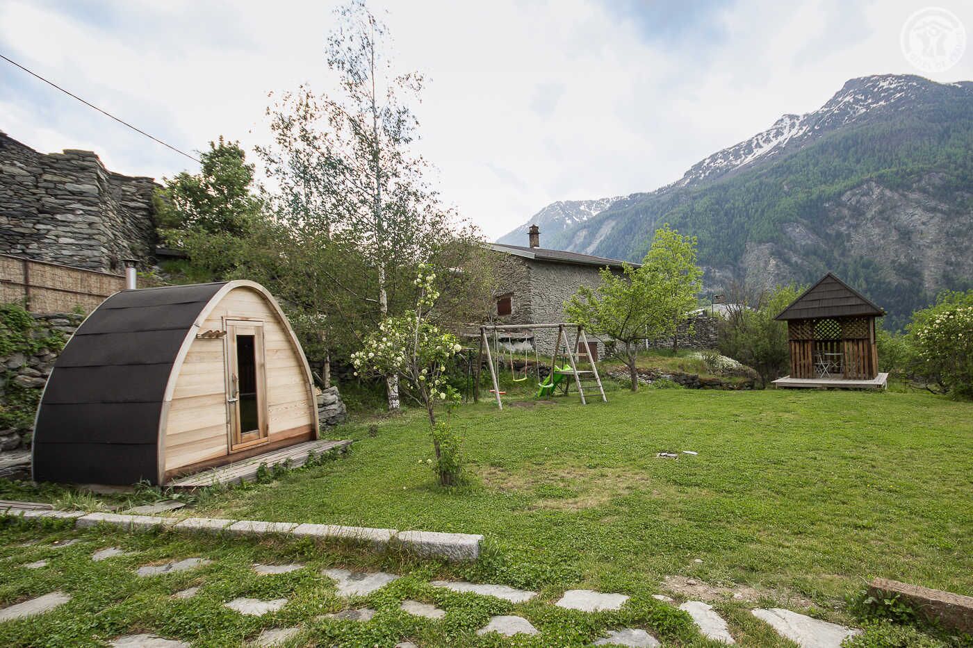 Een rustieke hut met een gebogen dak, een houten terras en een kleine tuin met een schommel.