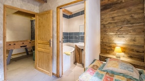 Een kamer met een houten deur, een badkamer met een wastafel en spiegel, en een bed met een quilt.