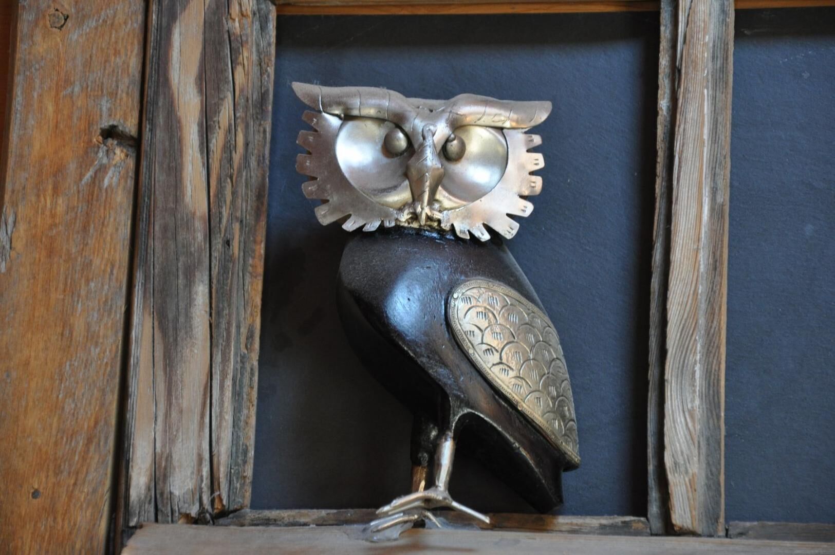A metal owl sculpture with intricate designs, placed in a wooden frame.
