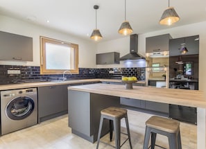 Une cuisine moderne dotée d’un îlot central, d’appareils électroménagers intégrés et de luminaires suspendus.