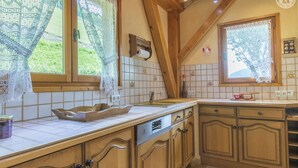 Una cocina con armarios de madera, lavavajillas integrado y una ventana con cortinas de encaje.