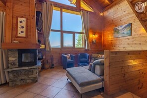 A cozy cabin interior with a stone fireplace, wooden walls, a large window, and a painting. - Chalet LE Dahu - Peisey-nancroix (PEISEY NANCROIX)