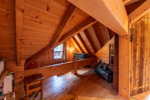 Un dormitorio de ático con techo inclinado, una ventana con cortinas, un banco de madera y un sofá colorido.