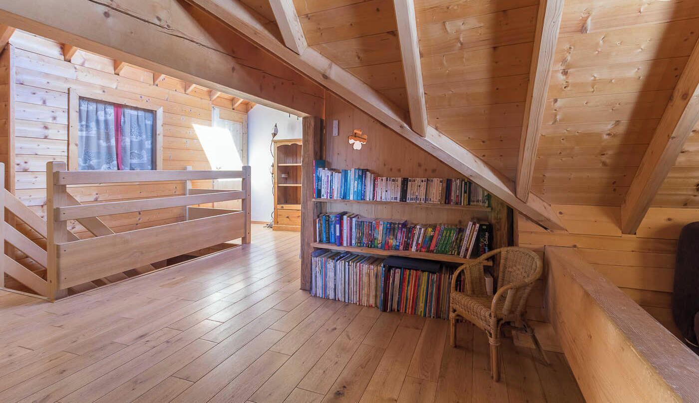 Un intérieur en bois avec un plafond en pente, un banc en bois, une bibliothèque et une chaise en osier.