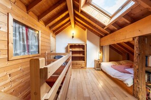 Interior de madera con techo inclinado, una litera, un escritorio y un ventanal.