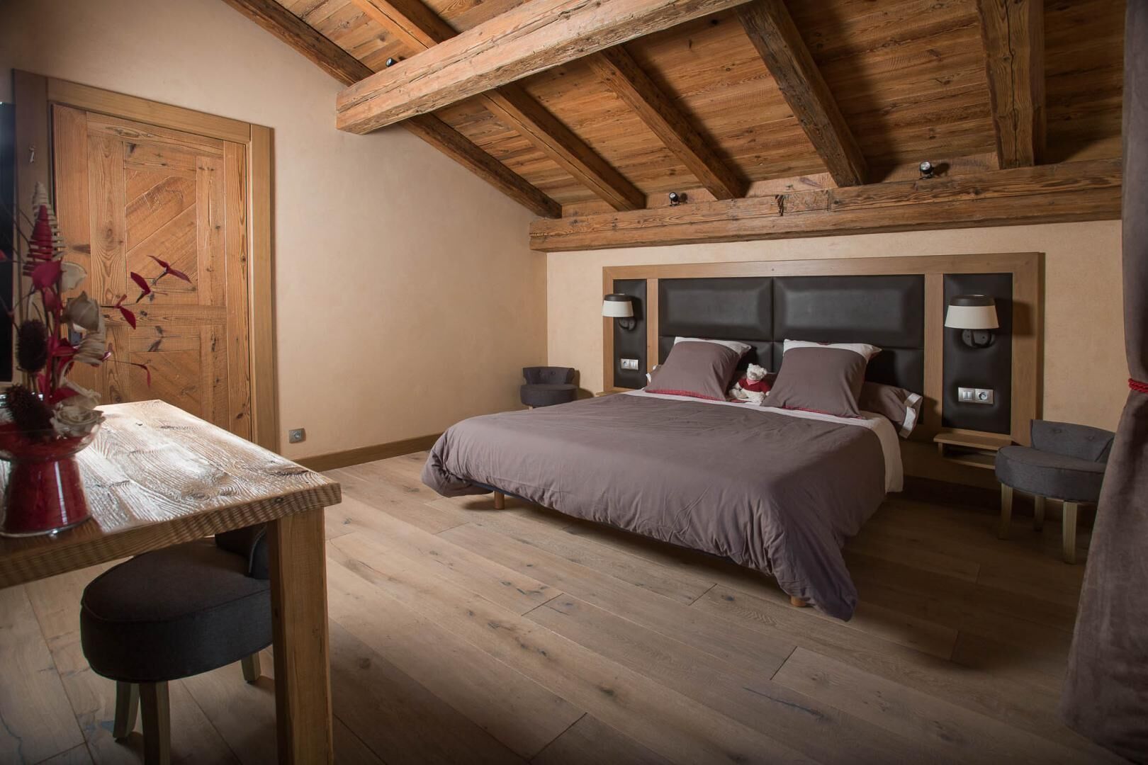 Un dormitorio con techo de madera, una cama con cabecera, mesitas de noche y un escritorio con silla.