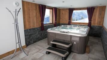 Un baño con jacuzzi, paredes de madera, detalles de piedra y vistas a las montañas.