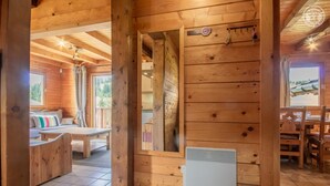 A wooden cabin interior with a dining area, a sofa with striped pillows, and a view of the outdoors. - LE Chomesi - Hauteluce-les-saisies (HAUTELUCE LES SAISIES)
