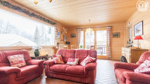 Una habitación acogedora con techo de madera, un sofá rojo, una mesa de comedor y vistas al exterior.