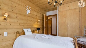 Un dormitorio de cabaña de madera con una cama, una cabeza de venado montada en la pared, dos apliques y una araña.