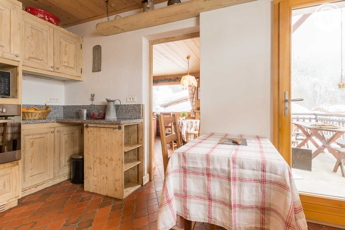Une cuisine avec des meubles en bois, un plan de travail en granit et une table recouverte d’une nappe à carreaux.