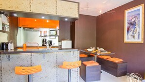 Cocina moderna con armarios color naranja, microondas y comedor con taburetes y una mesa dispuesta para dos.