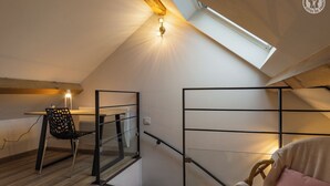 Ein Schlafzimmer im Loft-Stil mit schrägem Dach, einem Oberlicht, einem Bett, einem Sessel und einem Schreibtisch.