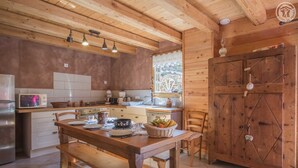 A rustic kitchen with wooden beams, a wooden table with a basket of fruit, and a large wooden door.