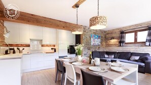 Una cocina moderna con armarios blancos, un comedor con mesa de madera dispuesta para cuatro personas y un sofá negro en la sala de estar.