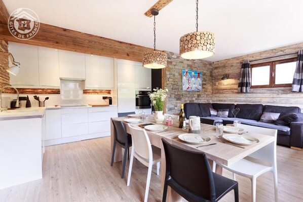 Una cucina moderna con mobili bianchi, un'area pranzo con tavolo in legno apparecchiata per quattro persone e un divano nero nella zona living.