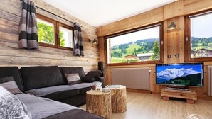 Una sala de estar acogedora con detalles de madera, un ventanal con vistas a la montaña, un sofá, una mesa de centro y un televisor de pantalla plana.