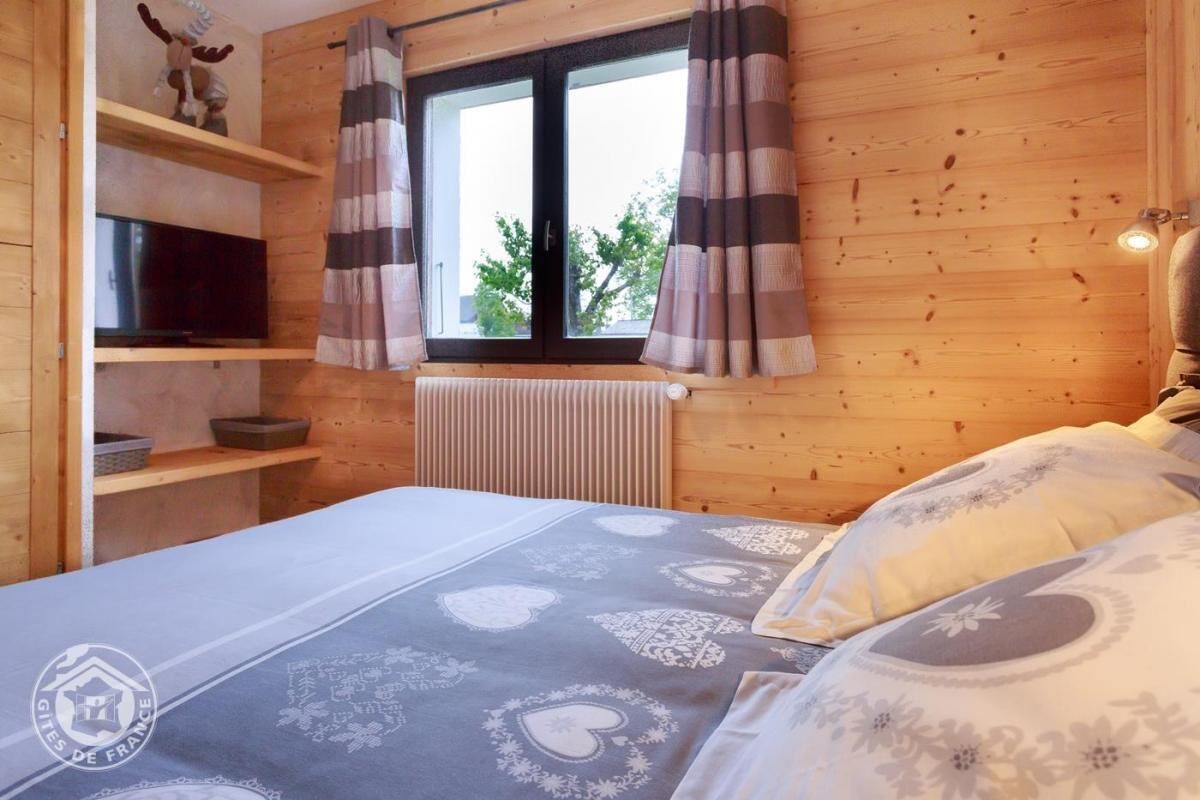 Une pièce confortable avec un lit, un téléviseur posé sur une étagère et une fenêtre avec des rideaux.