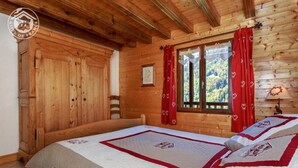 Une chambre rustique en bois avec deux lits, une armoire en bois, une fenêtre avec des rideaux rouges et un certificat encadré accroché au mur.