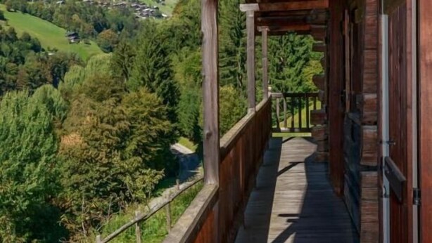 Un balcon en bois offrant une vue sur une vallée verdoyante et des collines.