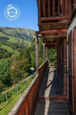 A wooden balcony with a view of a green valley and hills.