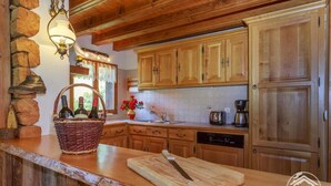 Une cuisine rustique avec des meubles en bois, un mur en pierre, un panier de bouteilles de vin et une planche à découper.