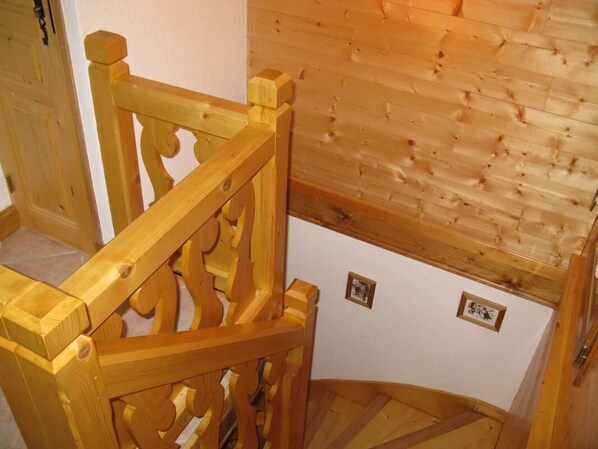 Una escalera de madera con diseño curvo que conduce a una habitación con pared de madera y dos pequeños marcos de cuadros.