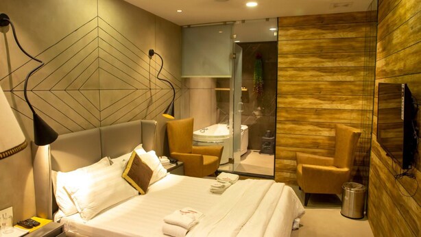 Une chambre d’hôtel moderne dotée d’un grand lit, d’un coin salon avec un fauteuil, d’une salle de bain avec une douche en verre et d’un mur décoratif en bois.