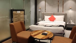 Une chambre d’hôtel avec un lit, deux chaises, une petite table en bois et une table de chevet avec une bouilloire.