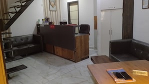 Un espace d’accueil comprenant un bureau en bois, un canapé en cuir noir, un sol en marbre et un escalier.