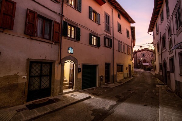 A narrow street with buildings on both sides, featuring a mix of architectural styles, including a building with a visible door and window shutters.