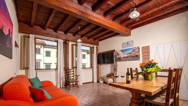 Un salon chaleureux avec un plafond en bois, un canapé orange vif, une table à manger avec des chaises et un téléviseur fixé au mur.