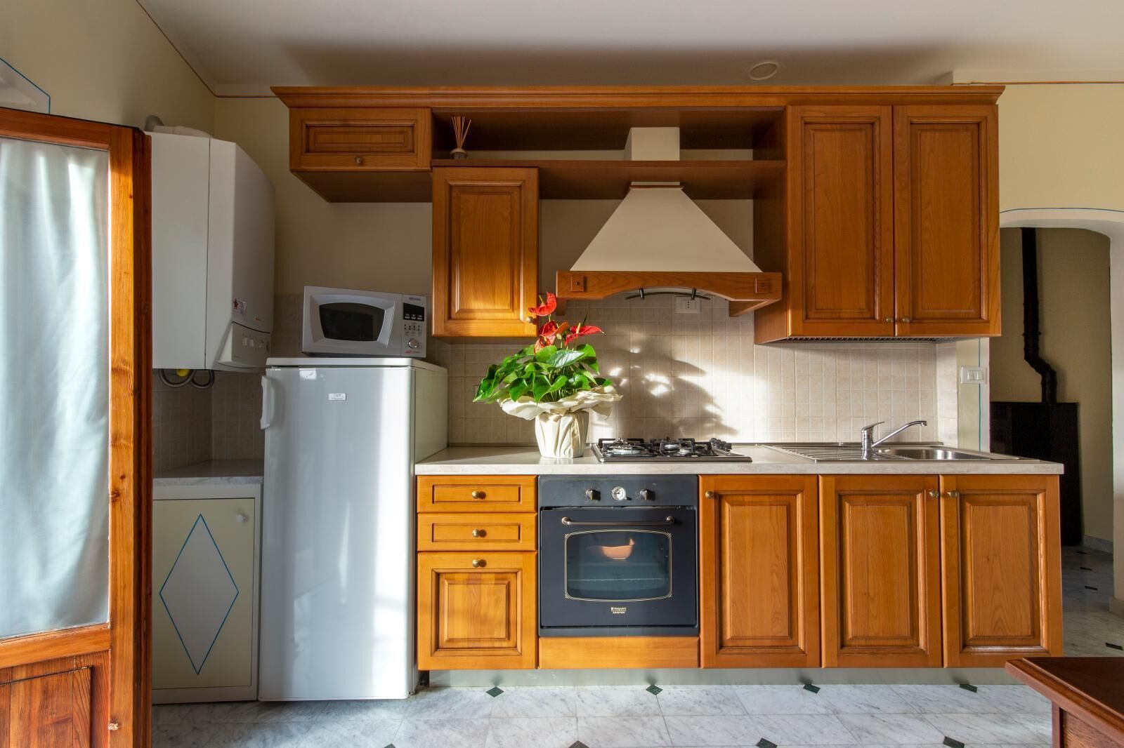 Una cucina compatta con mobili in legno, un frigorifero bianco, un forno a microonde, un fornello e un forno.