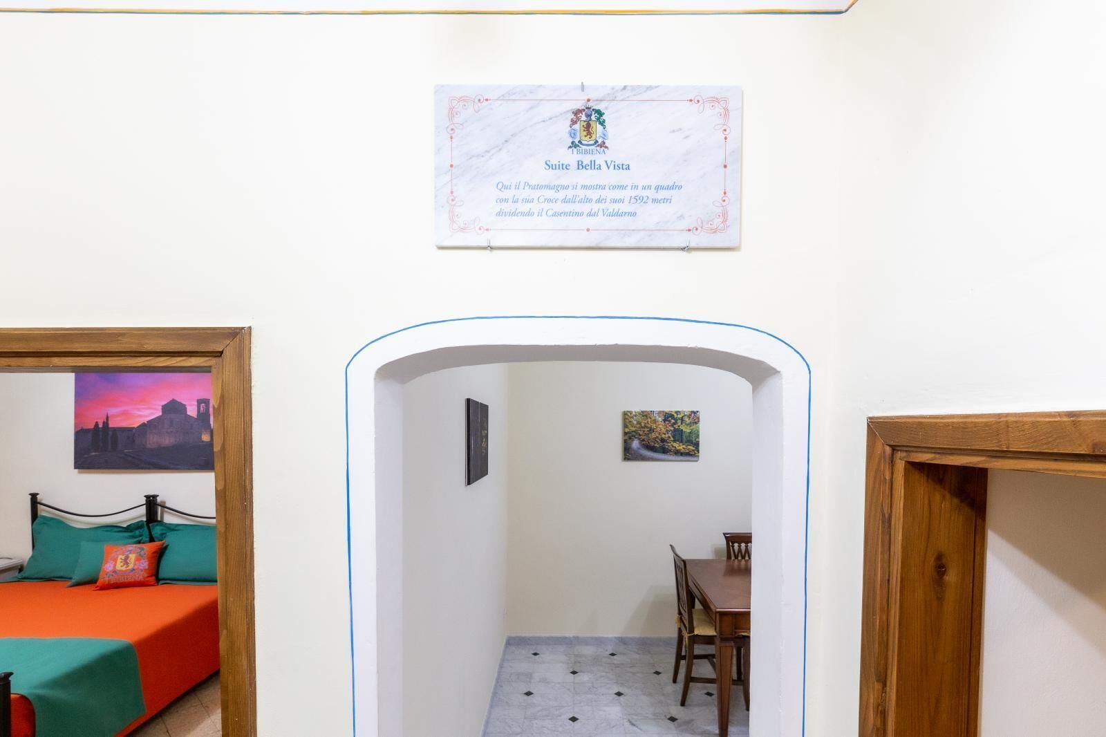 Habitación de hotel con cama, escritorio y silla. Hay un cuadro enmarcado en la pared y un cartel sobre la puerta.