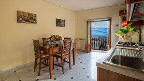 Un coin repas avec une table dressée pour deux personnes, une cuisine équipée d’une cuisinière à gaz et un balcon avec vue.