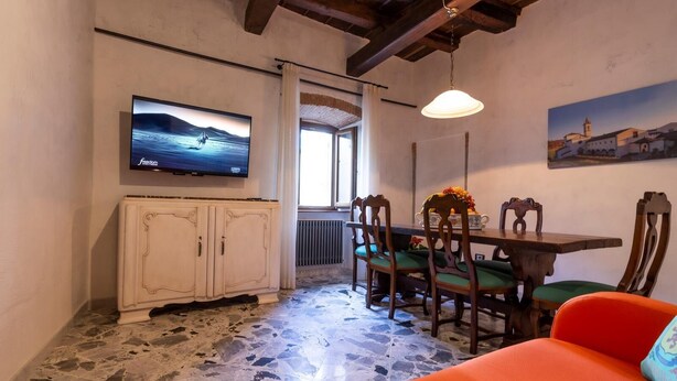A dining area with a table and chairs, a television mounted on the wall, and a painting on the wall. - The Bibiena Suites in the Historic Center (Bibbiena)
