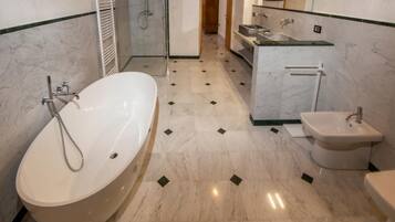 A modern bathroom with a large bathtub, a separate shower area, a bidet, and a vanity with a mirror.
