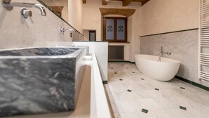 A modern bathroom with a large marble bathtub, a separate shower area, and a window with decorative glass. - The Bibiena Suites in the Historic Center (Bibbiena)