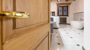 A wooden door with a brass handle, leading into a bathroom with a freestanding bathtub, a marble floor, and a radiator. - The Bibiena Suites in the Historic Center (Bibbiena)