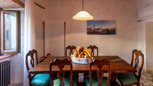 A dining area with a wooden table, green cushioned chairs, a fruit bowl, and a hanging light fixture. - The Bibiena Suites in the Historic Center (Bibbiena)