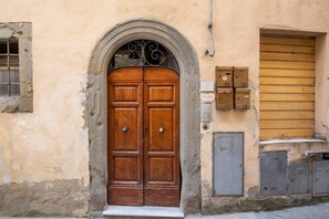 Une porte à deux battants en bois, surmontée d’une arche décorative, avec une boîte aux lettres et des boîtiers techniques fixés à la façade d’un bâtiment dont le revêtement est usé par le temps.