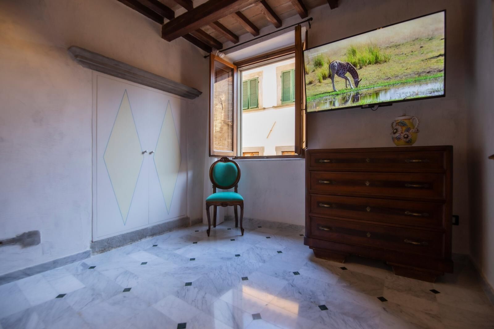 A room with a tiled floor, a wooden dresser, a chair, and a window with a painting of a giraffe.