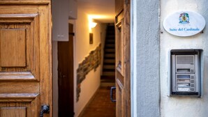 Eine Holztür, ein Flur mit einem an der Wand befestigten Schild, das „Suite del Cardinale“ zeigt, und ein Verteilerkasten mit einem Tastenfeld.
