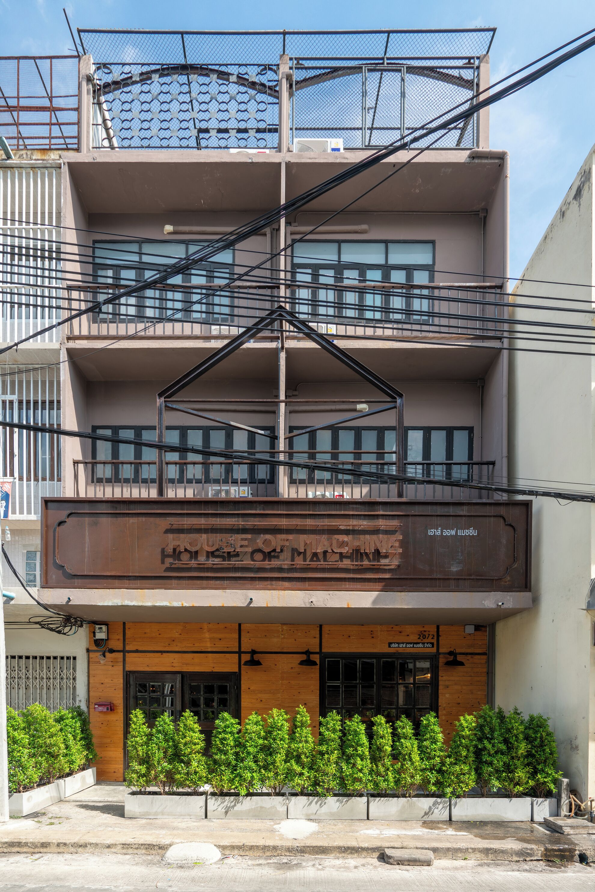A multi-story building with a sign reading "House of Machine." It features a wooden facade, multiple balconies, and a series of windows.