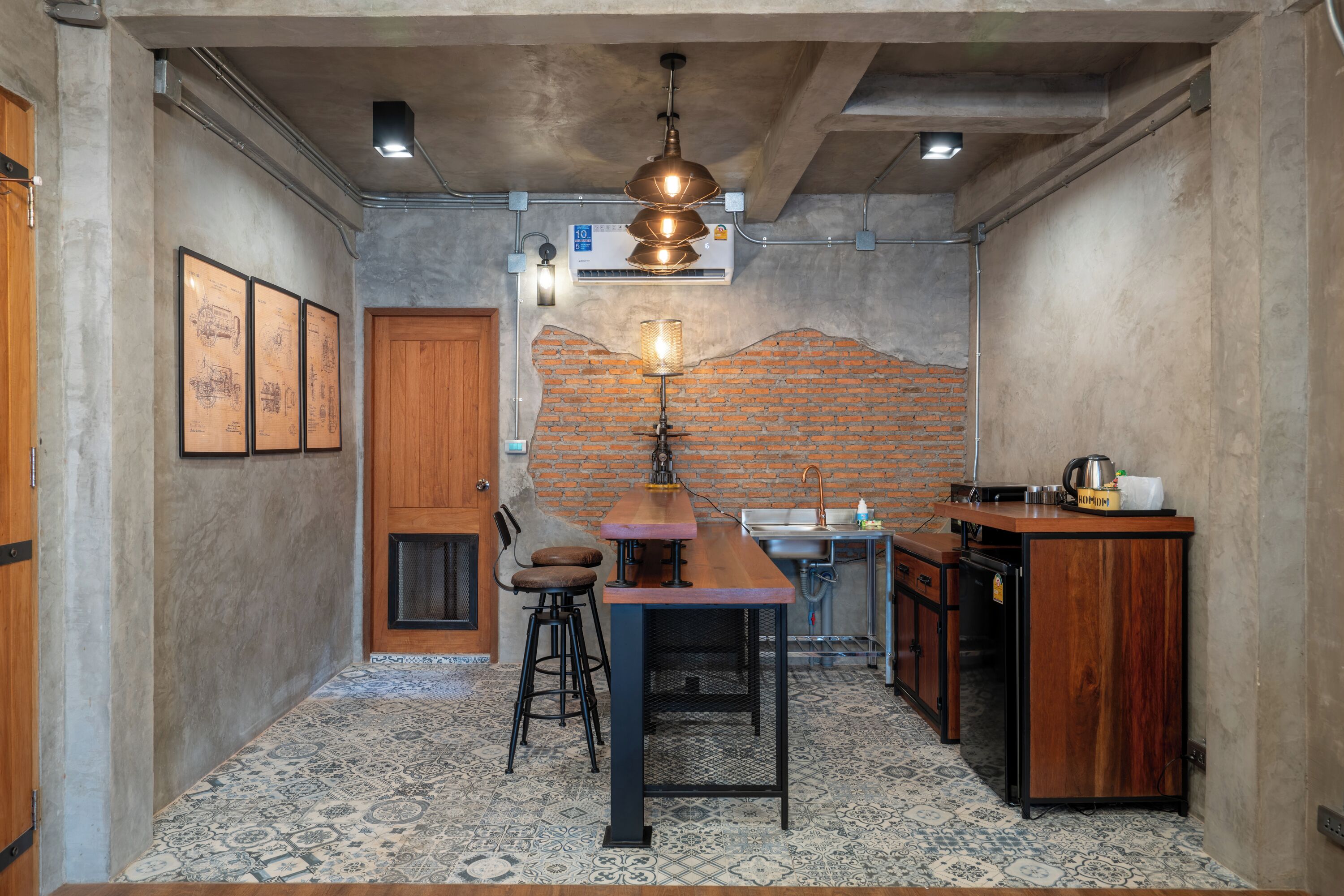 A compact kitchen with a wooden table, stools, a brick accent wall, and a sink.