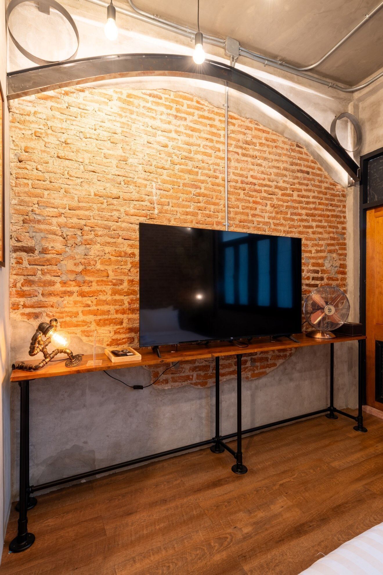 A modern living room with a brick wall, a flat-screen TV, a wooden coffee table, and a standing fan.