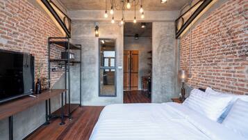 Un dormitorio moderno con pared de ladrillo, una cama de madera, un televisor sobre un mueble bajo y un escritorio con lámpara.